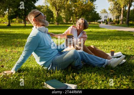 Senior loving family laughing while relaxing on green lawn grass in park Stock Photo