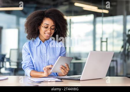 Young successful woman working with tablet computer inside office at workplace, smiling female programmer testing new app, writing code for software. Stock Photo