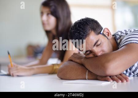 Tired, sleeping and a bored man in a classroom for learning, education and university burnout. Mental health, campus and a male student at a desk for Stock Photo