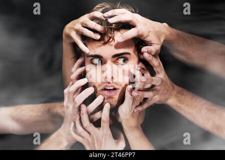 Scared, schizophrenia and man with hands, mental health or bipolar in studio isolated on a black background. Face, smoke and person with fear, horror Stock Photo