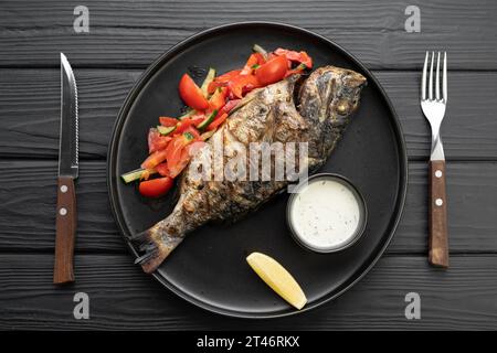 Grilled dorado with garnish on dark wooden background, top view. Composition with bbq fish and vegetables. Roasted dorado. Stock Photo