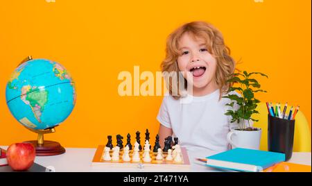 Excited kid play chess. Funny child. Chess game for kids. Intelligent, smart and clever school boy. Portrait of cute child play chess on studio Stock Photo