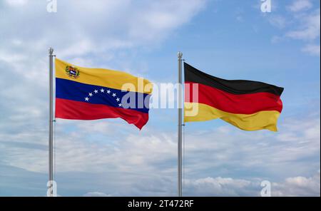 Germany and Venezuela flags waving together on blue cloudy sky, two country relationship concept Stock Photo