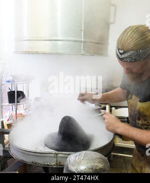 PRODUCTION - 24 October 2023, Thuringia, Altenburg: At Hut und Kostüm GmbH, milliner Thomas Krause works on a blank for a Biedermeier cylinder on a steam boiler, which is designed to produce a specific hat shape at around 100 degrees. The employees are currently working on various headwear items, such as historical chakos, bowler hats, top hats and hats for the upcoming carnival season. They are among the special productions currently in high demand for carnival associations, for uniforms for the Elferrat and clothing for dance marionettes. The small Altenburg company with ten employees is one Stock Photo