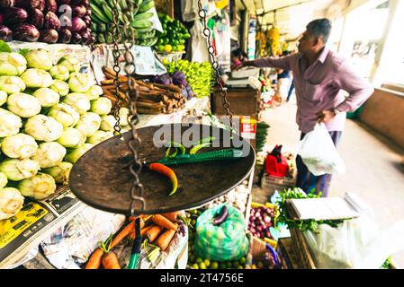 Chilis are on a weighing scale as a man picks some vegetables at a fruit and vegetable stall in the market in Kandy in Sri Lanka Stock Photo