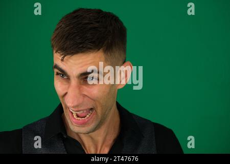 emotions of a handsome man guy on a green background chromakey close-up dark hair young man. Evil laughing of a man Stock Photo