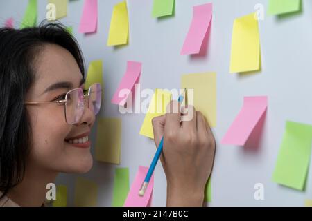 Creative woman writing on blank sticky notes on the wall Stock Photo