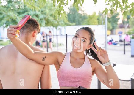 young latina taking a selfie after training. woman sitting next to an unrecognizable man with her back turned. Stock Photo