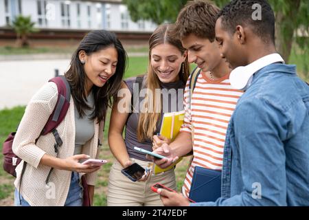 Diverse group of friends checking their phones.Happy multiracial friends using smartphone in a campus. Stock Photo