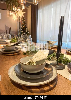 table settings, dinner table with plates and wine glasses for noel dinner in a living room with Christmas decorations and ornaments. empty clean plate Stock Photo