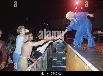 At a live concert, country music superstar Dolly Parton goes to the front of the stage to shake hands with fans. At a venue on her 1978 Midwest concert tour. Stock Photo