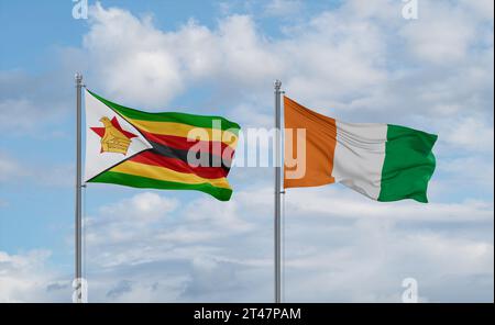 Zimbabwe and Ivory Coast flags waving together in the wind on blue ...