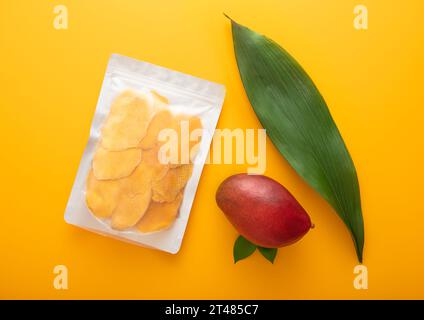 Large pack of dried mango slices with leaf and raw fruit on yellow background.Top view. Stock Photo