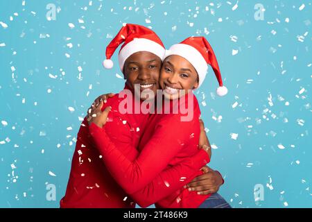 Black Couple In Santa Hats Hugging Under Falling Confetti, Studio Stock Photo