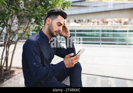 Stressed Middle Eastern business guy using app on phone outside Stock Photo