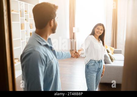 Young Indian couple holding hands, smiling in a cozy living room setting Stock Photo