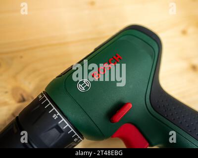 Bosch logo sign on a green cordless drill tool. The electric device for craftsmen is lying on a wooden table. It is equipment in a garage workshop. Stock Photo