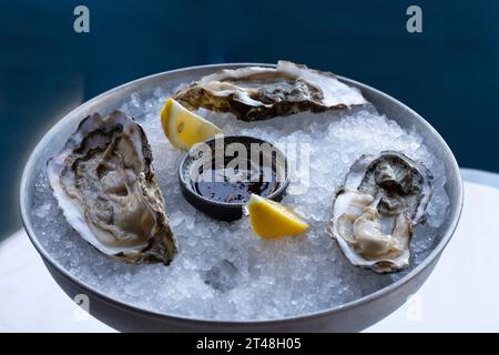 Fresh oysters on the halves of the shell are served in a plate with ice, lemons and sauce. The concept of healthy nutrition. Stock Photo