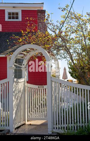 White trellis gate leading to red Cape Cod style cottage on Provincetown harbor Stock Photo