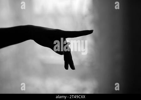 Monochrome shot of a hand with a ring, silhouetted against a blurred curtain, evoking feelings of longing and anticipation. Stock Photo
