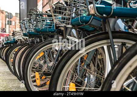 Row lined up of bicycles for hire by the public at a rental station on the sidewalk. Close-up of wheel and bicycle basket in the centre of Dublin, Ireland Stock Photo