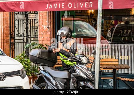 A young woman in the helmet is checking her mobile phone alongside her motorbike. Stock Photo