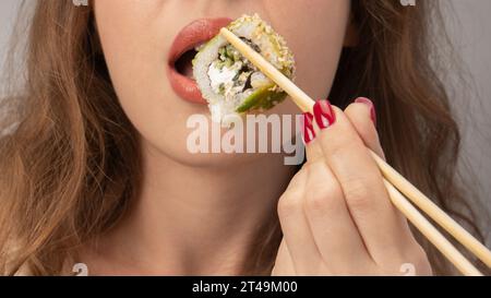 Young woman with red nails is eating sushi close up. Stock Photo