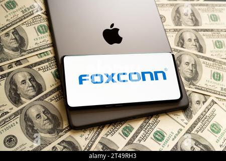 FOXCONN logo seen on smartphone, Apple logo seen on IPad and US dollar bills around. Concept. Stafford, United Kingdom, October 29, 2023 Stock Photo