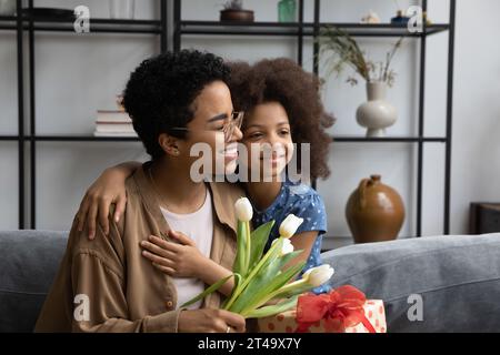 Happy mom receiving gift and bunch of flowers from daughte Stock Photo