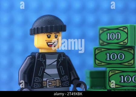 Tambov, Russian Federation - October 29, 2023 A Lego burglar minifigure standing near a pile of money against a blue baseplate background Stock Photo