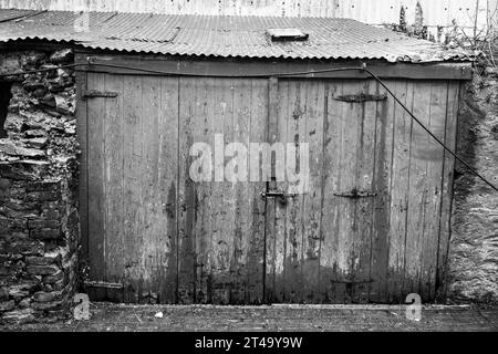 Ramshackle shed, shot in black and white, with vertical wood panelled doors between stone walls, found just off Island Street, Salcombe. Stock Photo