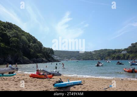 View of busy beach at Mill Bay, East Portlemouth, on a summer's day, looking toward South Sands with blue sky and white whispy clouds. Stock Photo