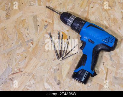 Close up of electric drill and drill bits on old wooden table. On left side is empty space to put text or something else. This file is cleaned and ret Stock Photo