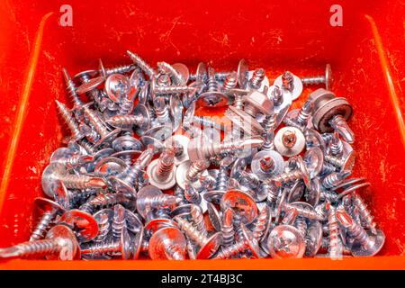 Small screws with drills and large heads for metal in a red plastic container close-up Stock Photo