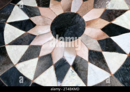 Rounded Handmade Cowhide Fur Carpet in patchwork style. Detail of stitched together fur blocks of brown, beige and dark brown colors. Homemade round l Stock Photo