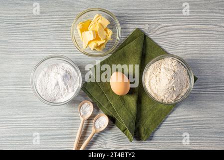 On a wooden table: baking ingredients, green napkin, wooden spoons, baking soda, dry yeast. Top-down view in a flat lay. Stock Photo