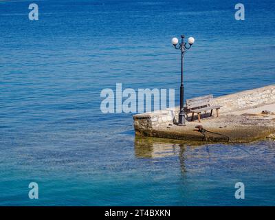 Jetty bench and street lamp in the pretty little fishing harbour of Kouloura on the north-east coast of Corfu in the Ionian Islands of Greece Stock Photo