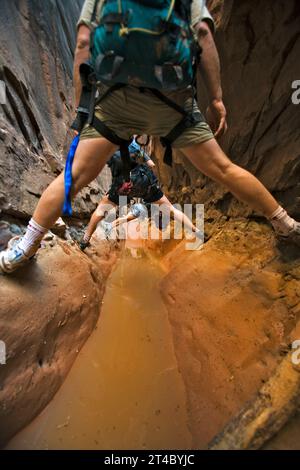 Three people stemming between two walls above water in slot canyon, Utah. Stock Photo
