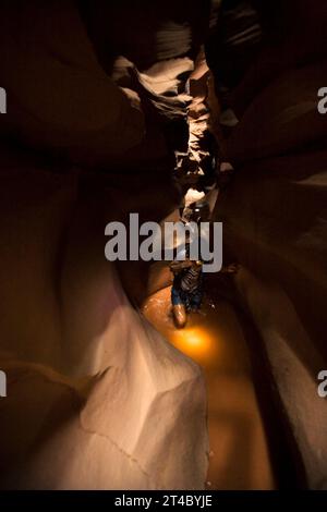 A woman in dark canyon wading through water with headlamp on, Utah. Stock Photo