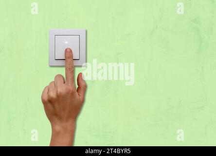 Female finger on light switch close-up, green background. Stock Photo