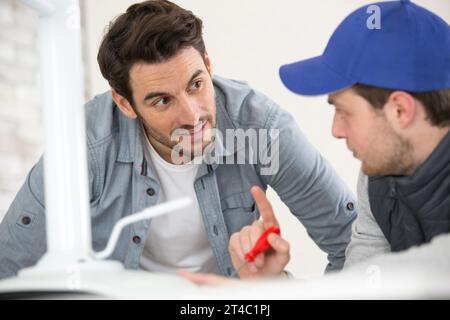 engineer helping male apprentice in factory to measure component Stock Photo