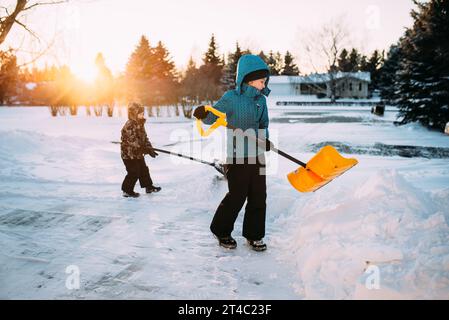 Young boy and girl in snowsuit push heavy snow in driveway with Stock Photo