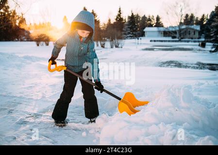 Young girl pushes heavy snow in driveway with shovel  with sun f Stock Photo