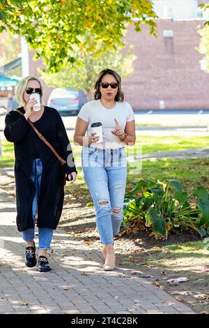 Two women in their 30s walking outside talking, drinking coffee Stock Photo