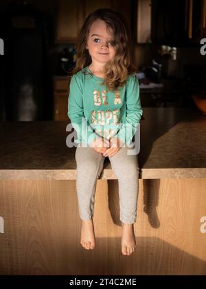 Beautiful little girl with blonde curls smiling in kitchen Stock Photo