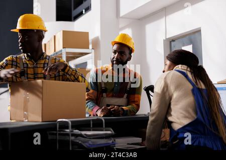Mail sorting center african american workers team preparing parcel for delivery. Postal service employees register received package at counter desk in post office storage room Stock Photo