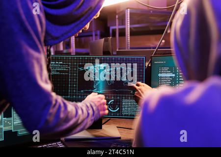 Hackers using spyware on computer screen while working together. Two criminals in hoods cracking password and checking confidential information on internet server in hideout Stock Photo