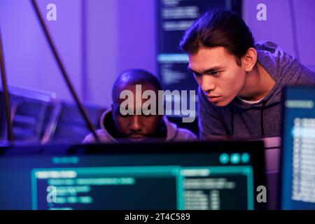 Hackers analyzing and discussing malicious code on computer screen, planning internet crime. Two criminals talking about scam scheme and doing illegal activity late at night Stock Photo