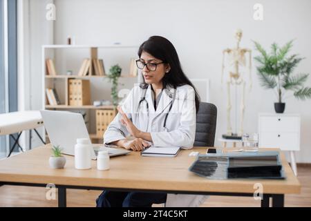 Doctor waving hello while having video call via laptop Stock Photo