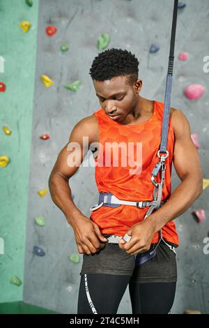 handsome young african american man checking his safety rope before climbing up wall, bouldering Stock Photo